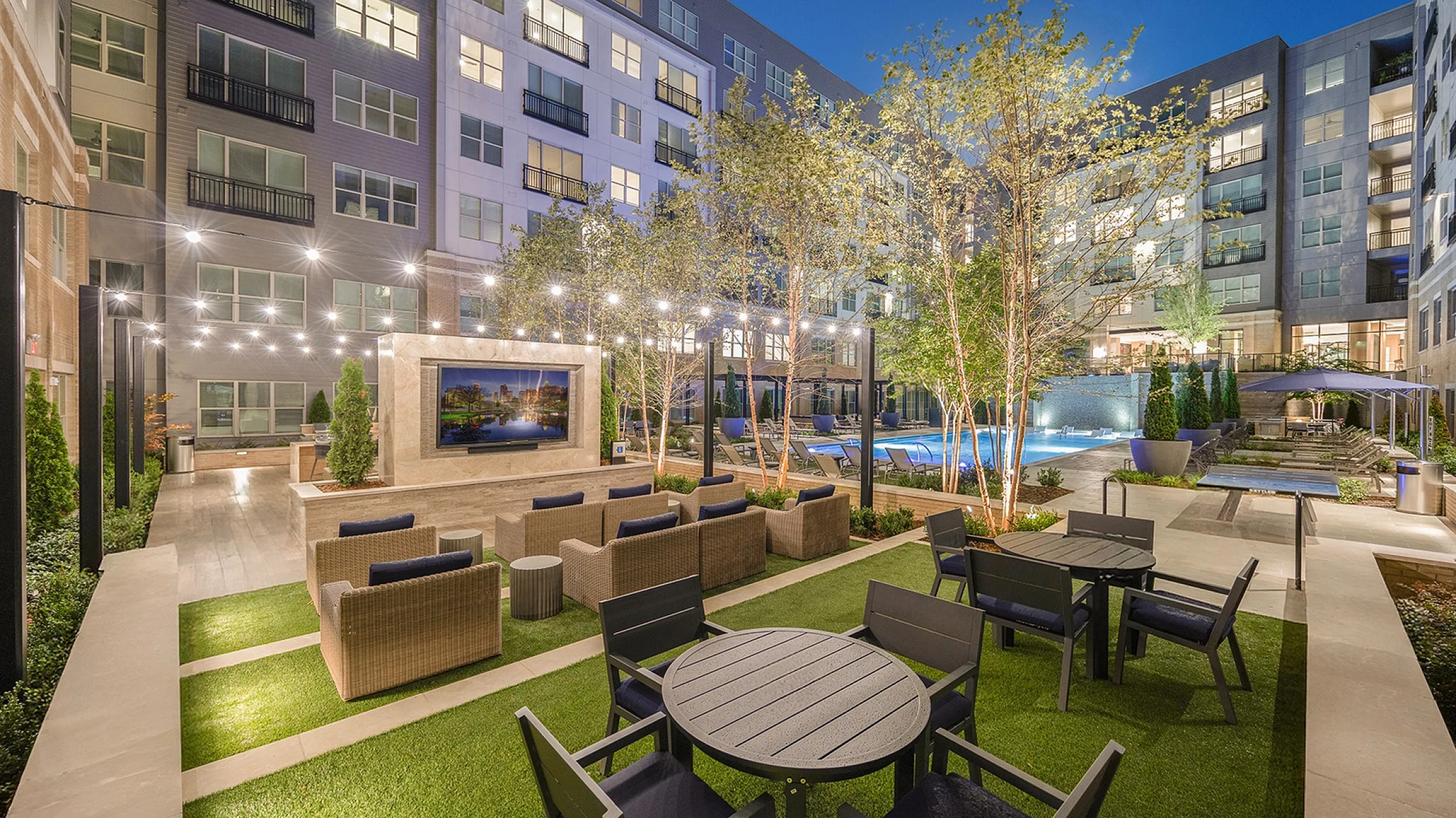 Luxurious outdoor courtyard featuring elegant seating areas, string lighting, and a poolside retreat in a modern apartment complex.