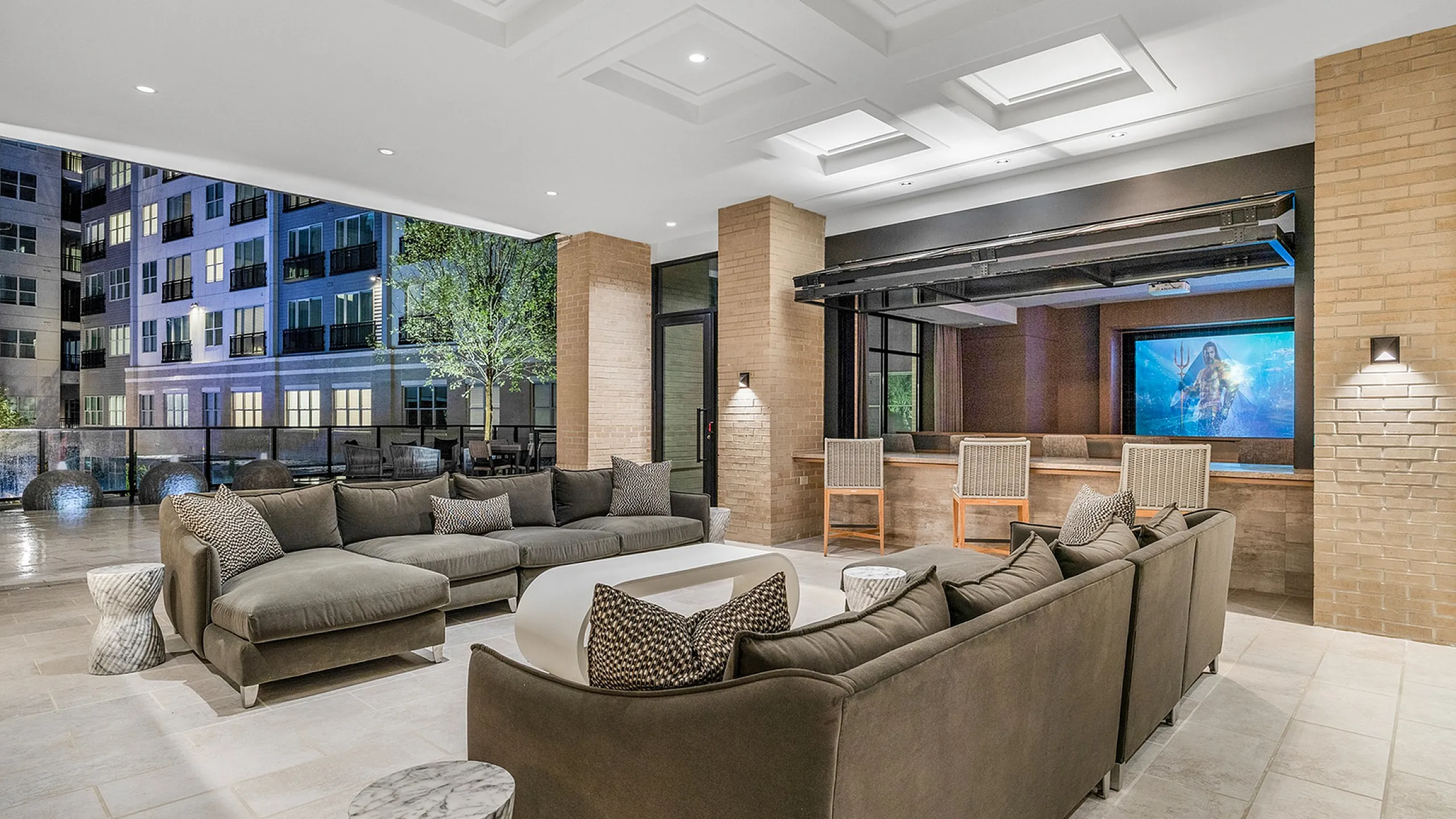 Luxurious open-concept living space featuring plush sofas, modern bar area, and large screen display with serene cityscape view.