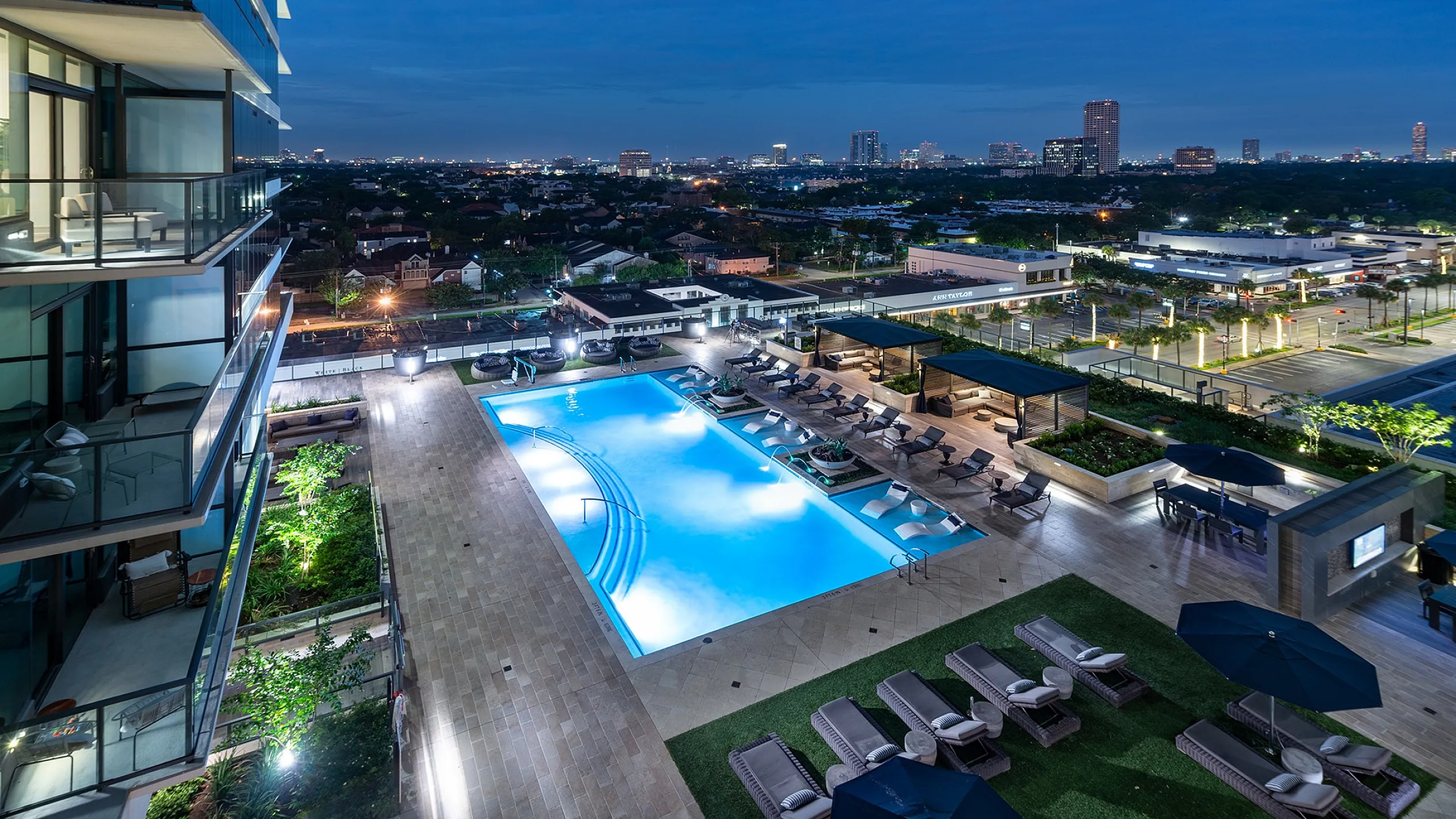 Luxurious apartment balcony view of a sparkling pool and vibrant city skyline at night, offering a perfect blend of urban living and relaxation.