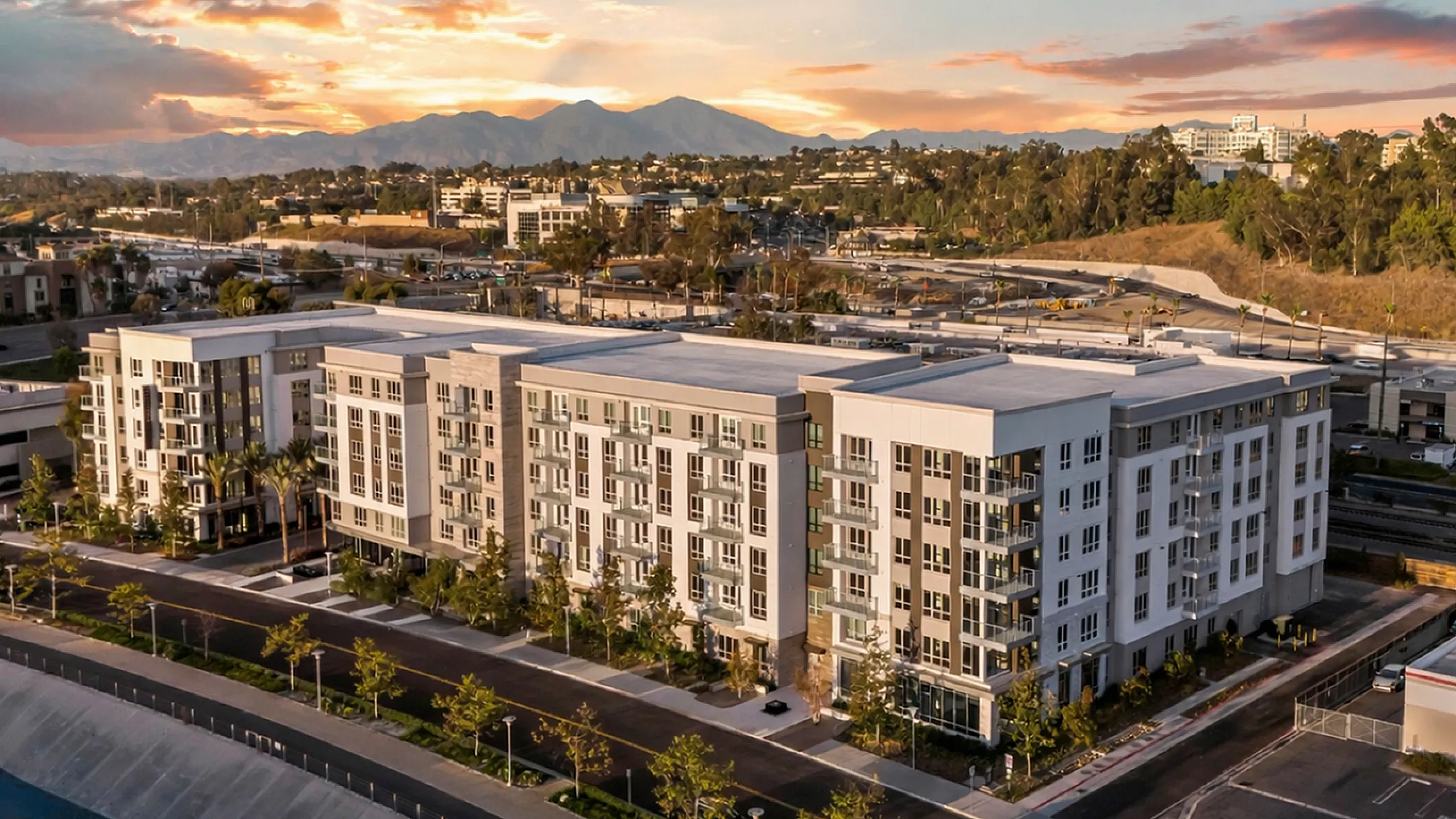 Modern apartment complex with a scenic mountain backdrop and vibrant sunset, showcasing elegant urban living.