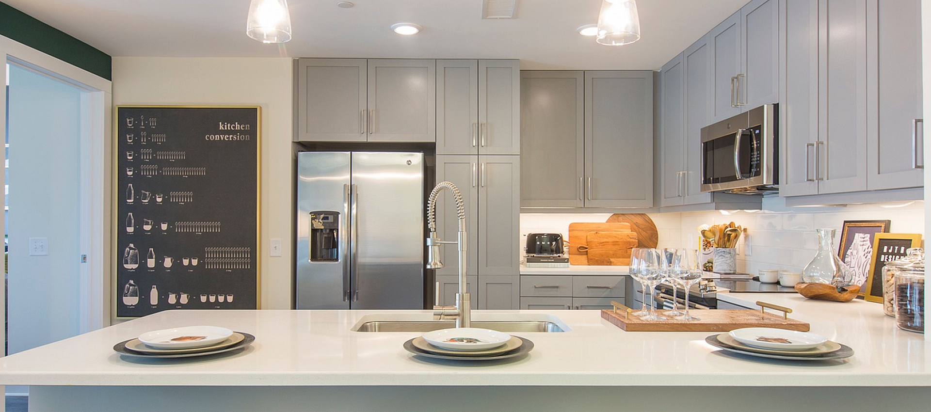 Modern kitchen with sleek gray cabinetry, stainless steel appliances, and elegant pendant lighting over a pristine white island, creating a stylish and inviting cooking space.