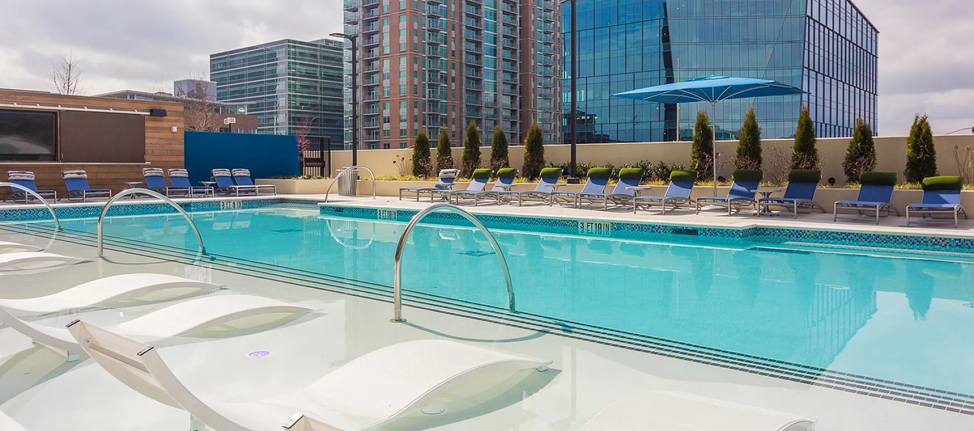 Elegant rooftop pool with modern lounge chairs against a stunning city skyline backdrop, perfect for relaxing and enjoying urban views.