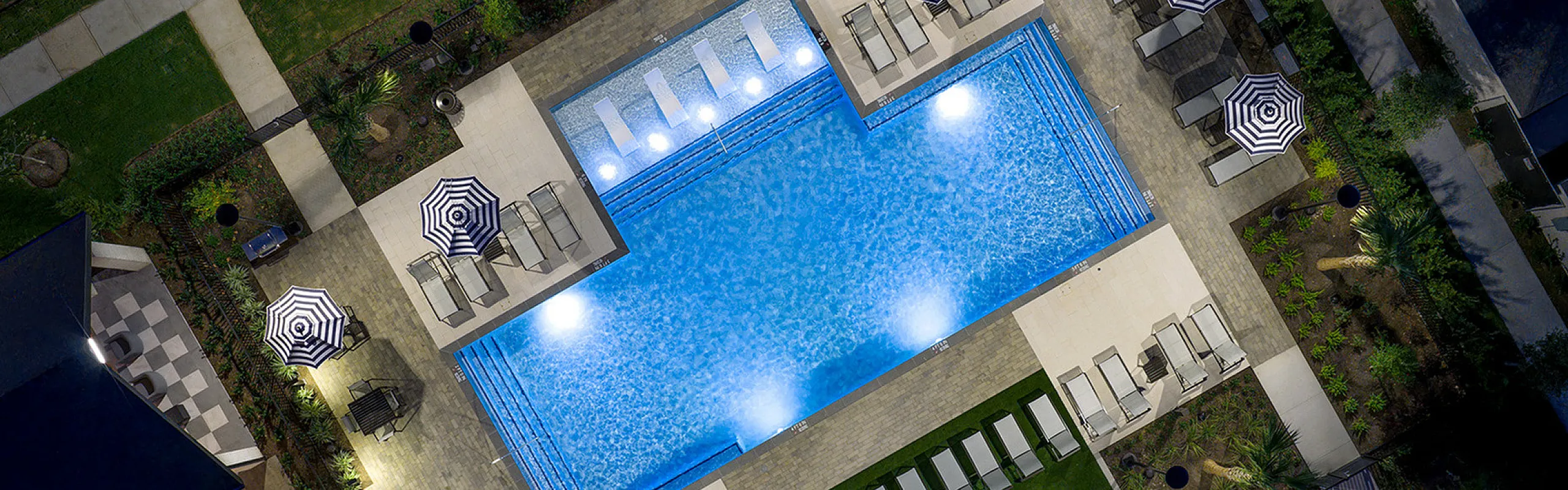 Luxurious rooftop pool with elegant striped umbrellas and comfortable lounge chairs, surrounded by lush greenery for a perfect urban oasis.