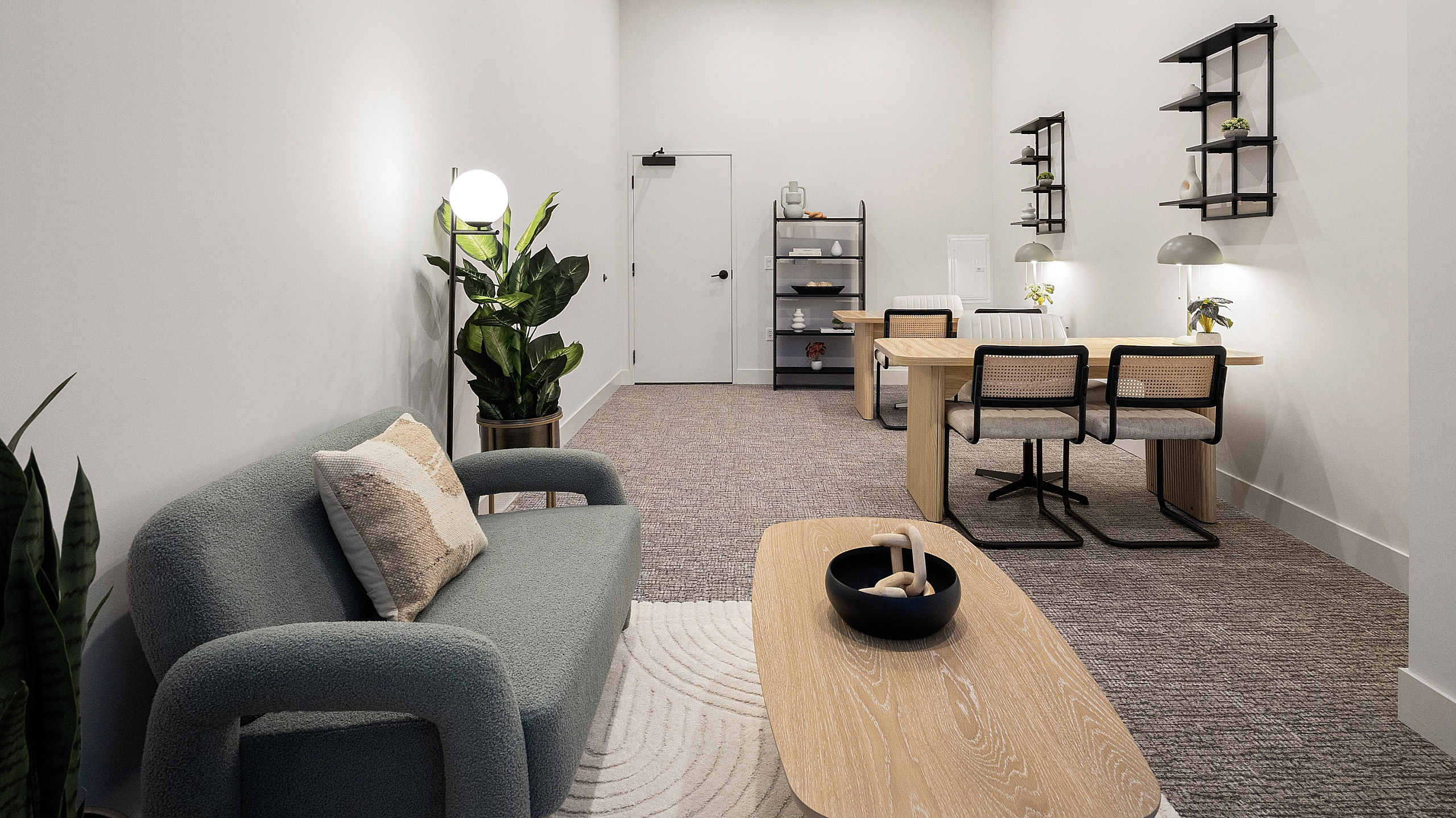 Contemporary apartment interior featuring a cozy lounge area with a stylish sofa, chic wooden coffee table, and lush green plants, leading to a modern workspace with elegant shelving and ample lighting.