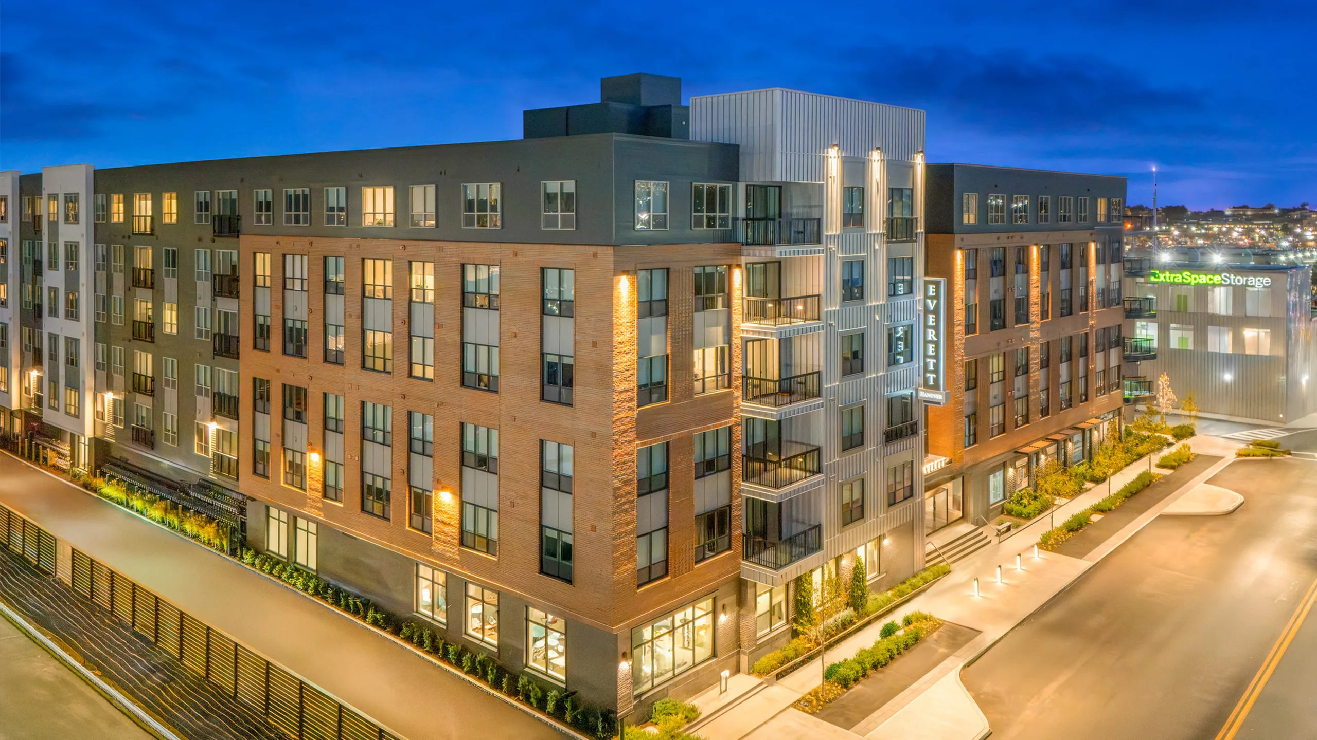 Modern apartment complex with sleek architectural design, illuminated at dusk, featuring large windows and inviting balconies.
