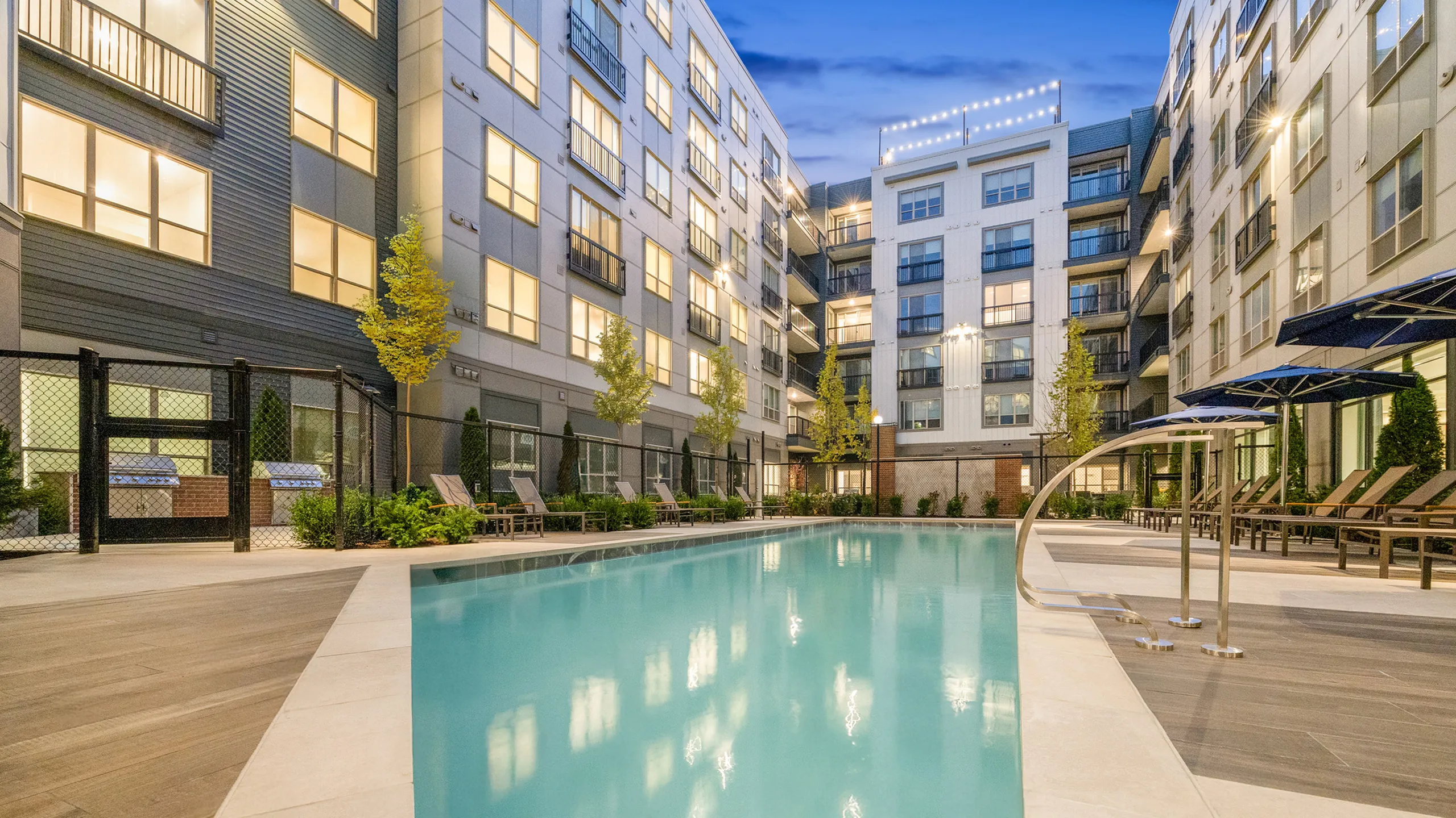 Luxurious apartment courtyard featuring a sparkling pool, elegant lounge chairs, and modern architectural design.