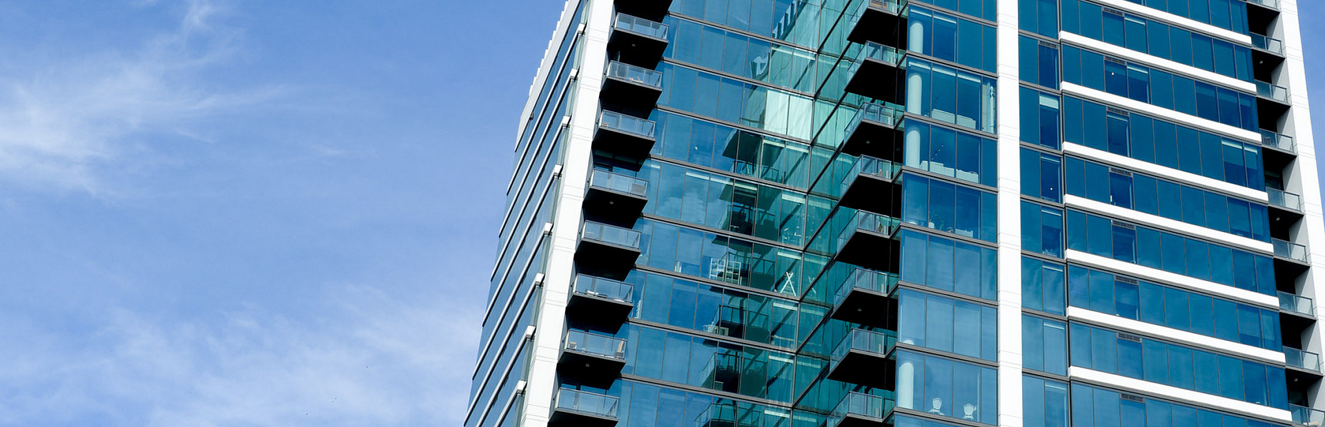 Modern glass skyscraper against a clear blue sky, featuring sleek architecture and balconies for an urban lifestyle.