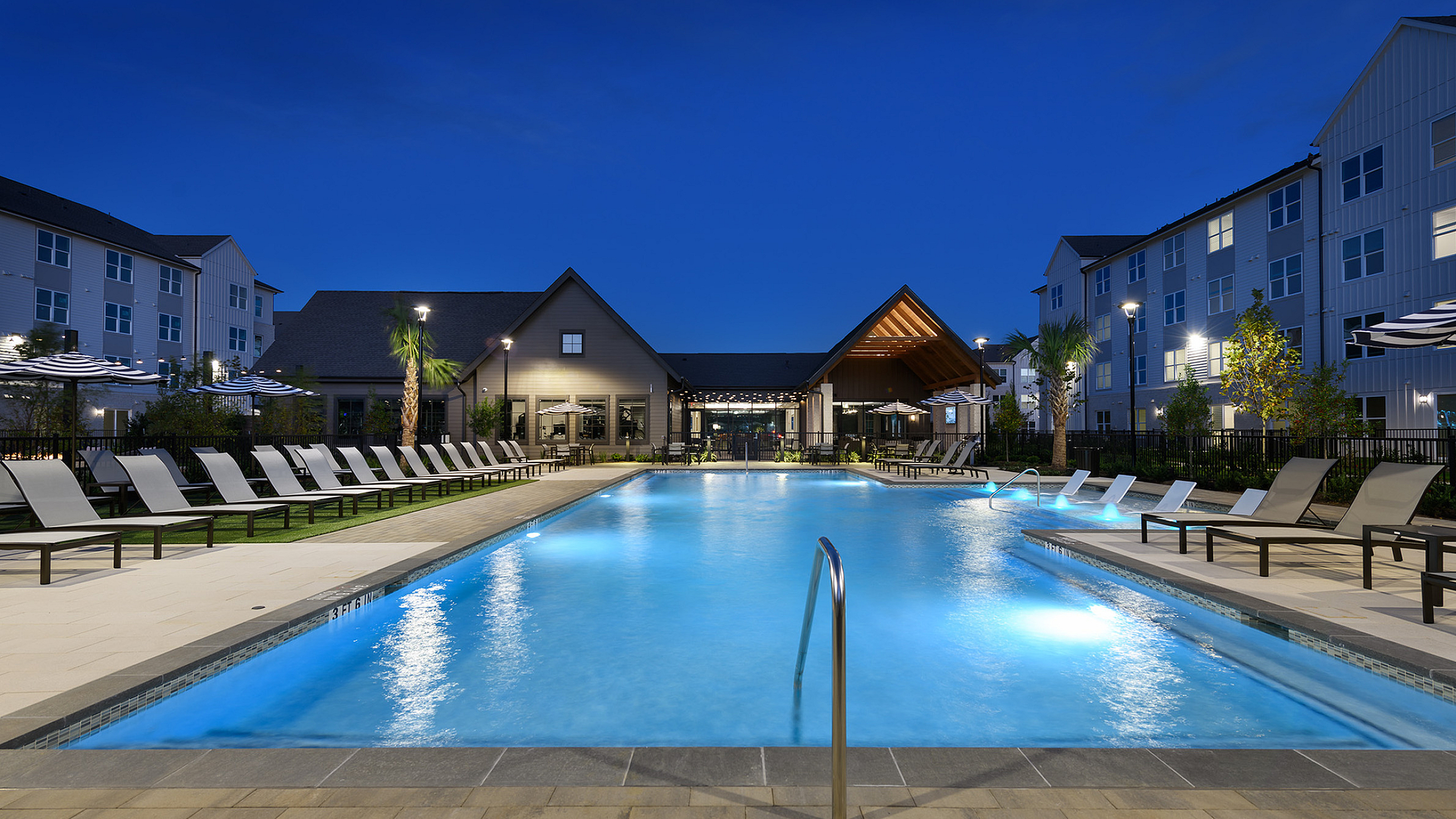 Captivating night view of a luxurious swimming pool surrounded by stylish lounge chairs at a modern apartment complex.