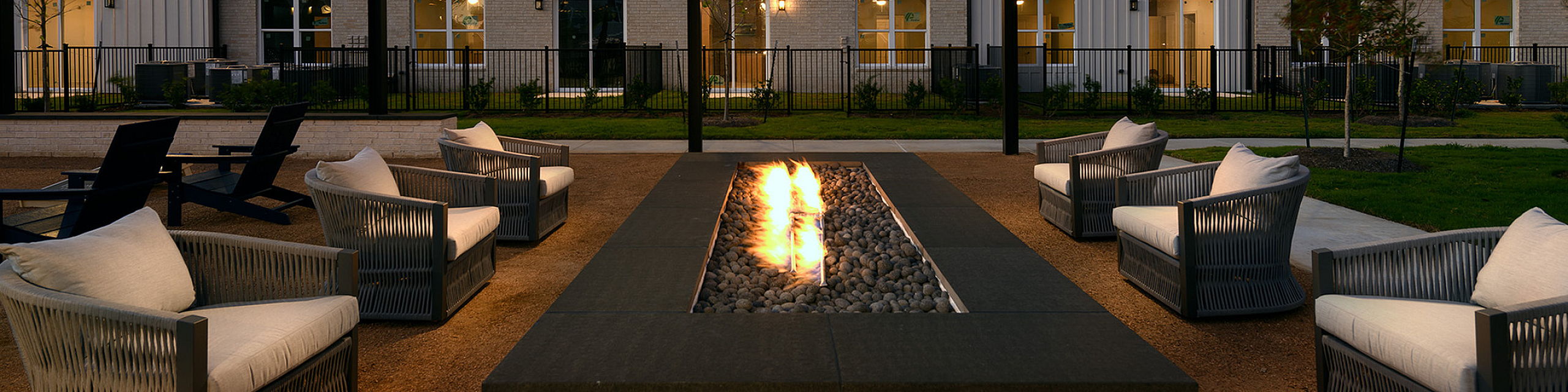 Inviting courtyard with elegant fire pit surrounded by cozy seating, set against modern multi-story apartment building, perfect for evening relaxation.