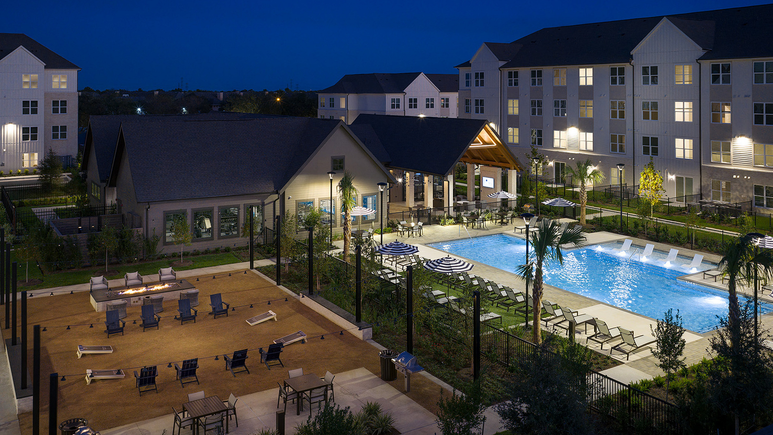 Luxurious apartment community with modern architecture, featuring illuminated swimming pool and cozy recreational area at night.