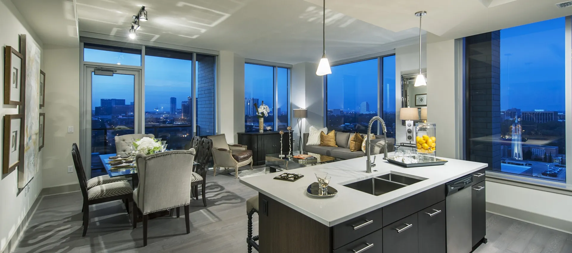 Modern open-concept apartment with a chic kitchen island, elegant dining area, and panoramic city views through floor-to-ceiling windows.