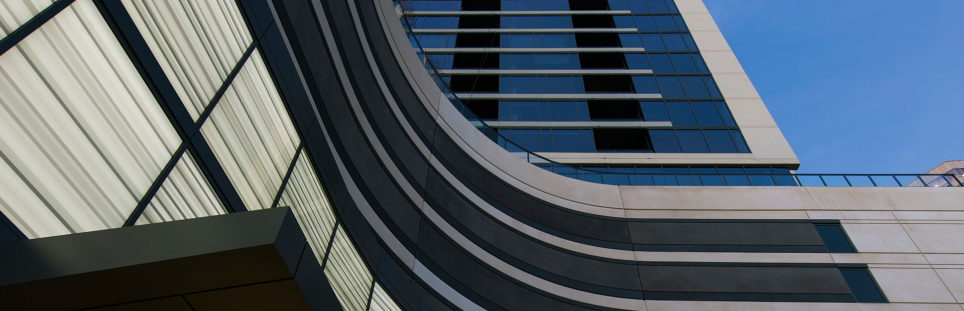 Modern high-rise apartment building with sleek architectural design and expansive glass windows against a clear blue sky.