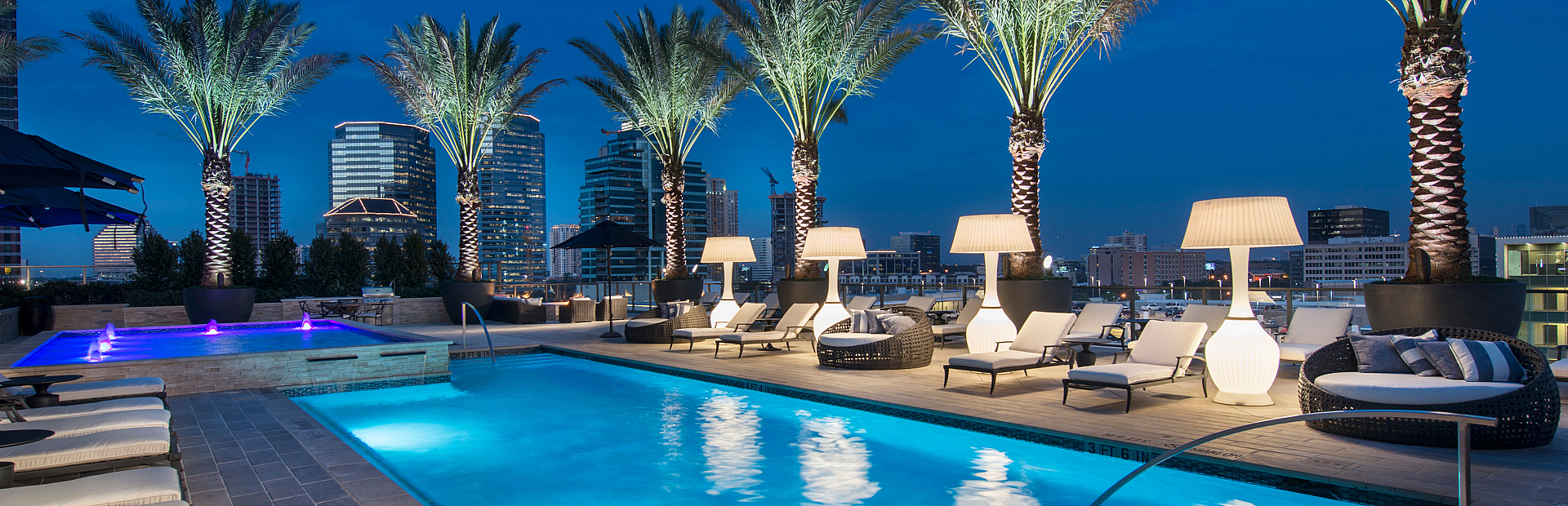 Luxurious rooftop pool oasis with palm trees, elegant loungers, and stunning city skyline views at dusk.