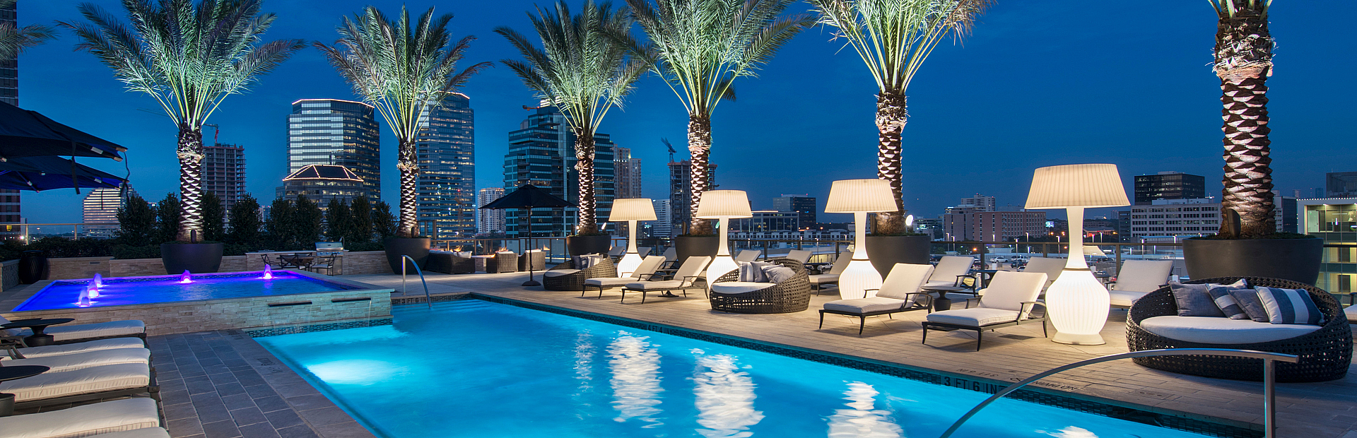Luxurious rooftop pool with stunning city skyline views, elegant loungers, and illuminated palm trees creating an exquisite night ambiance.