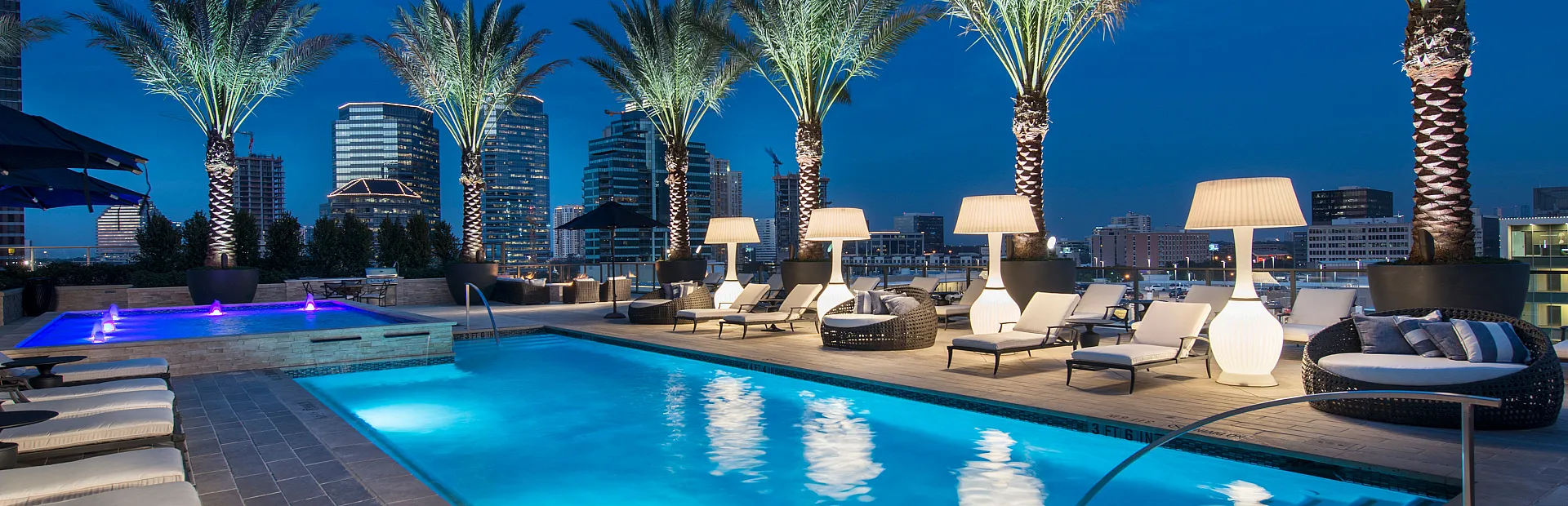 Luxurious rooftop pool area illuminated at night, featuring elegant palm trees and stunning cityscape views.
