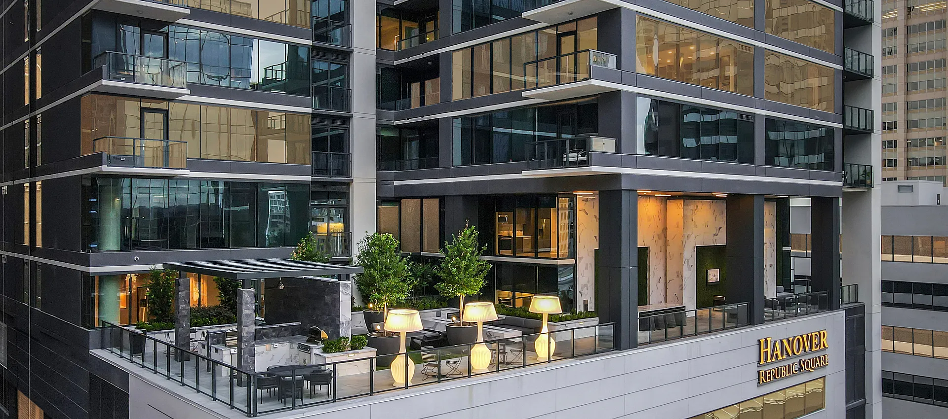 Modern high-rise building with stunning glass facade and luxurious rooftop terrace featuring greenery and ambient lighting.