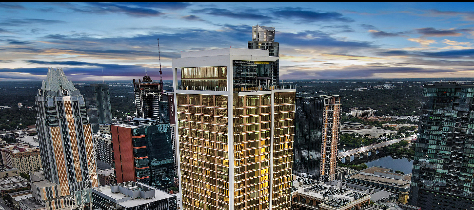 Stunning aerial view of a modern cityscape featuring a luxurious high-rise apartment building with a rooftop pool and breathtaking skyline view at sunset.