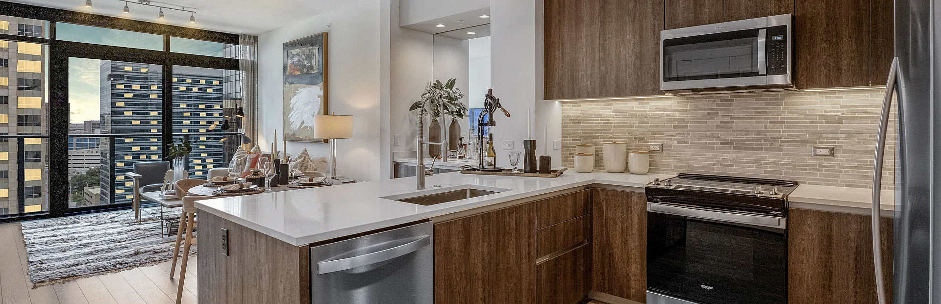 Modern apartment interior featuring a sleek kitchen with stainless steel appliances, and a cozy living area with city views through large windows.
