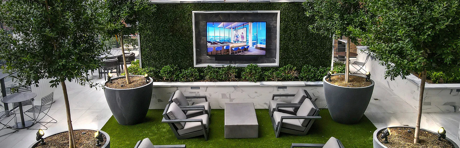 Chic outdoor lounge with plush seating, surrounded by lush greenery and modern urban scenery.
