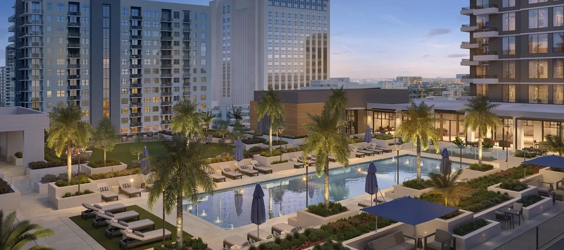 Luxurious apartment complex with illuminated pool and lush palm trees at sunset, offering elegant outdoor seating and stunning city views.