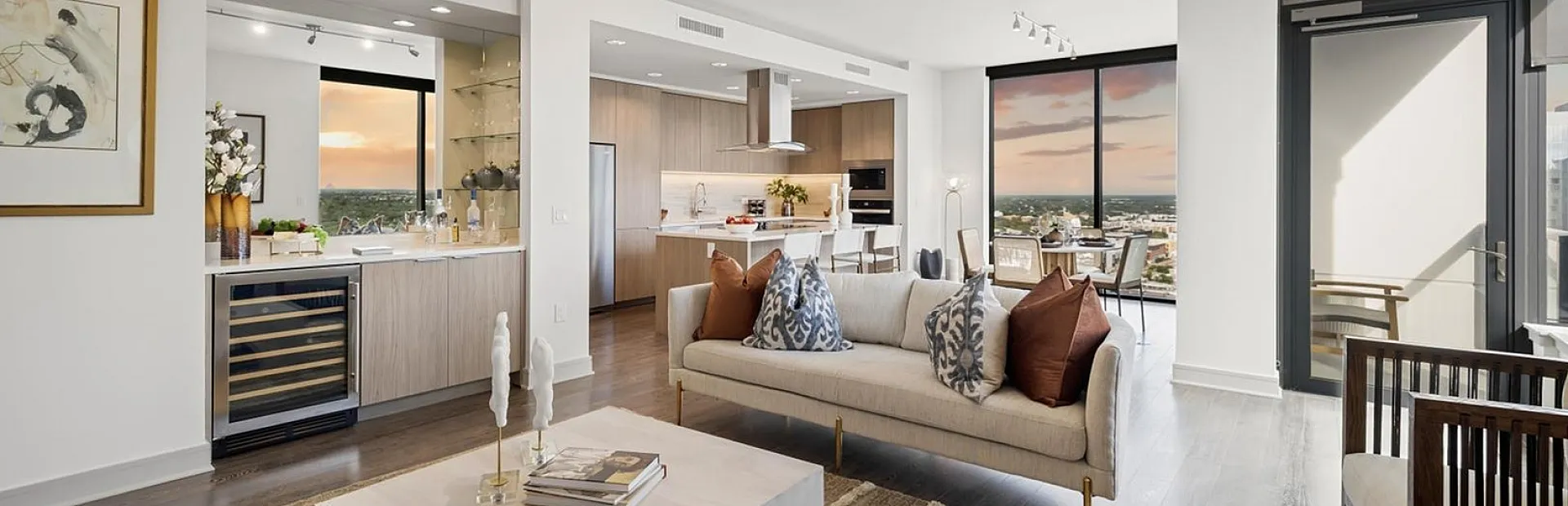 Luxurious open-concept living room with modern d&eacute;cor, panoramic windows offering stunning sunset views, and a stylish kitchen with sleek appliances.
