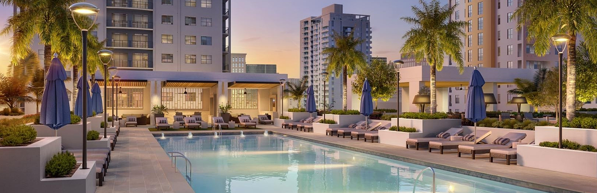 Luxurious apartment complex featuring a sparkling pool, elegant poolside seating, and tropical palm trees at dusk.