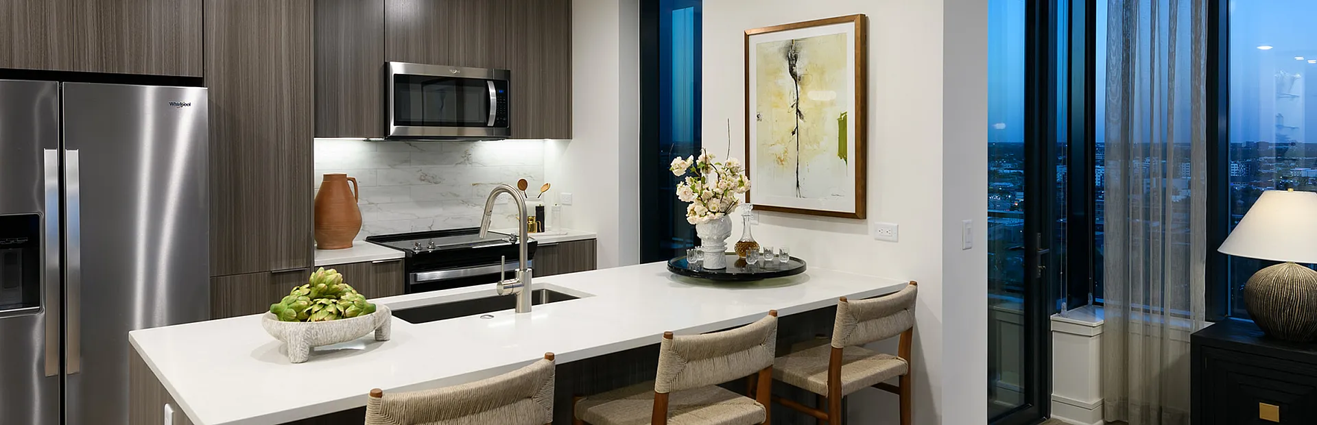 Elegant kitchen with modern appliances, sleek island with seating, and large windows offering stunning city views.