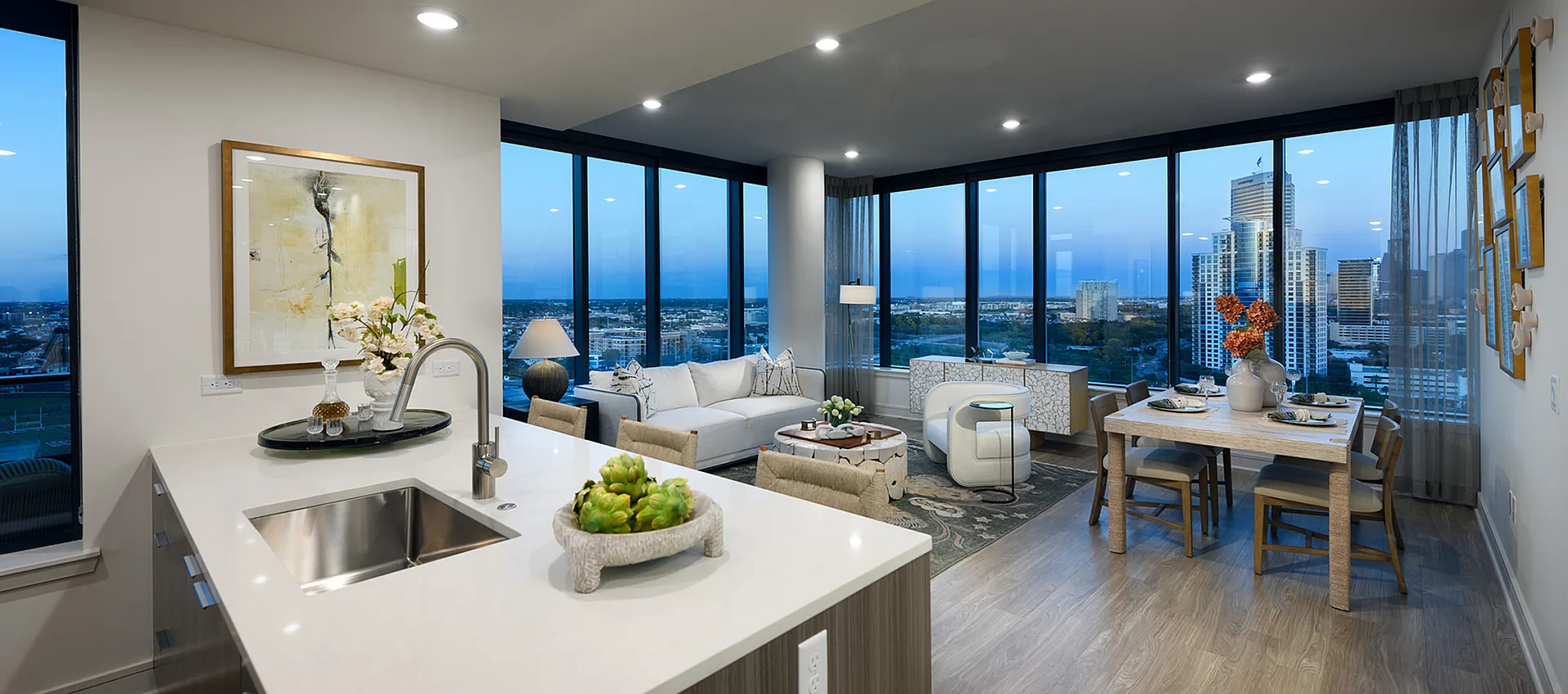 Contemporary open-plan apartment with large windows offering breathtaking city views, modern kitchen island, and elegant living and dining areas.