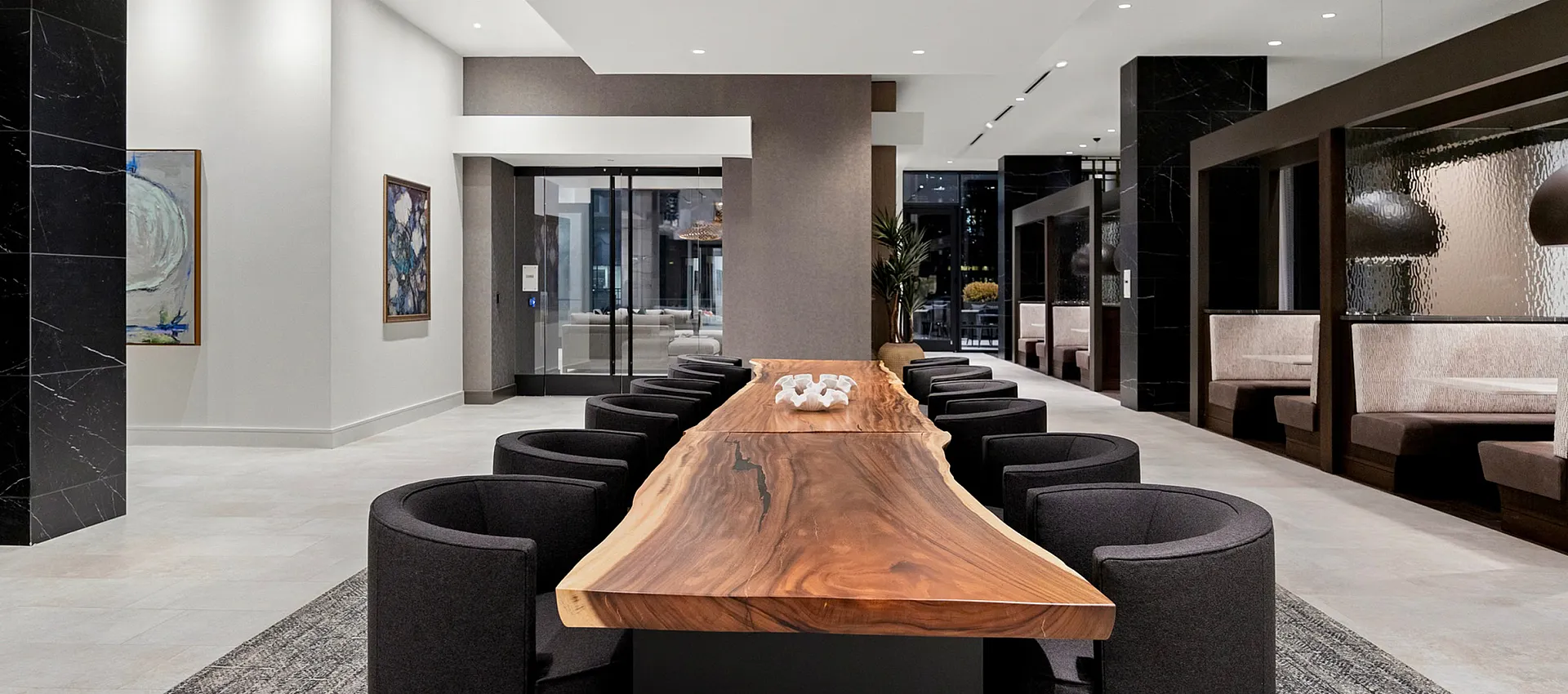 Elegant and modern communal space featuring a stunning natural wood dining table, surrounded by sleek black chairs, perfect for sophisticated gatherings.