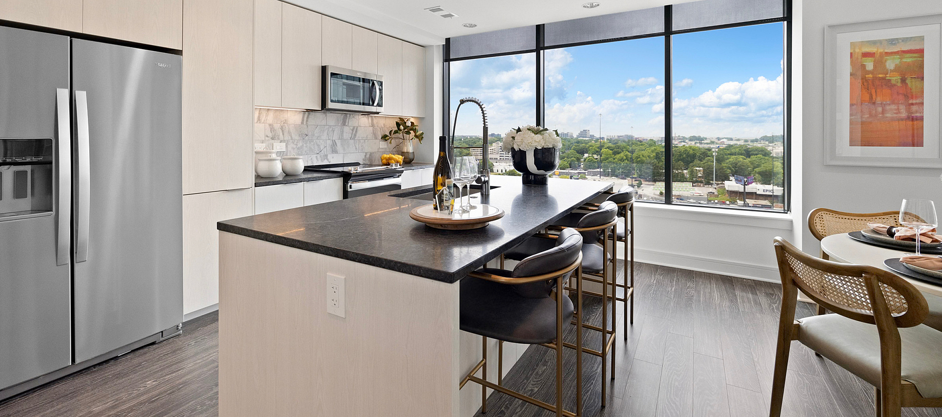 Sleek modern kitchen with stainless steel appliances, large island seating, and stunning city skyline views through expansive windows.