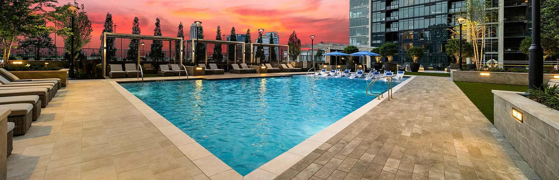 Luxurious modern apartment complex with a stunning outdoor pool area under a vibrant sunset sky.