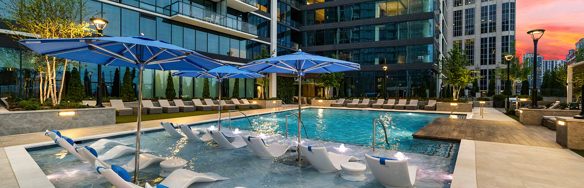 Luxurious urban oasis showcasing a stunning pool area with elegant lounge chairs and vibrant blue umbrellas, surrounded by modern high-rise architecture at sunset.