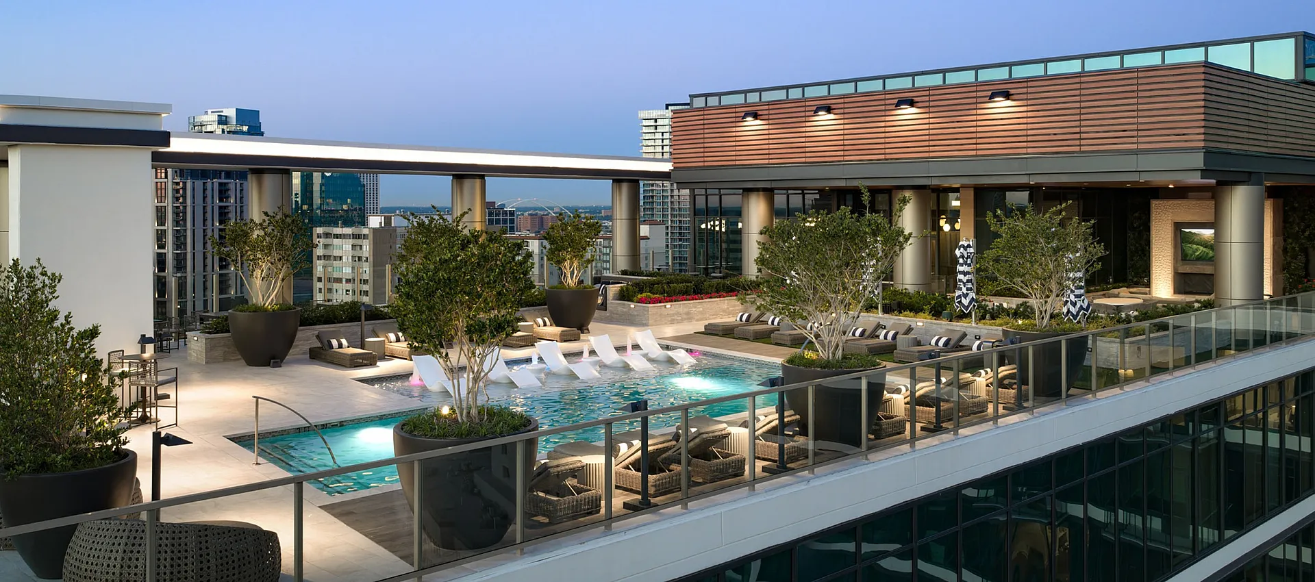 Luxurious rooftop terrace featuring a sparkling pool, chic lounge areas, and lush greenery with panoramic city views.
