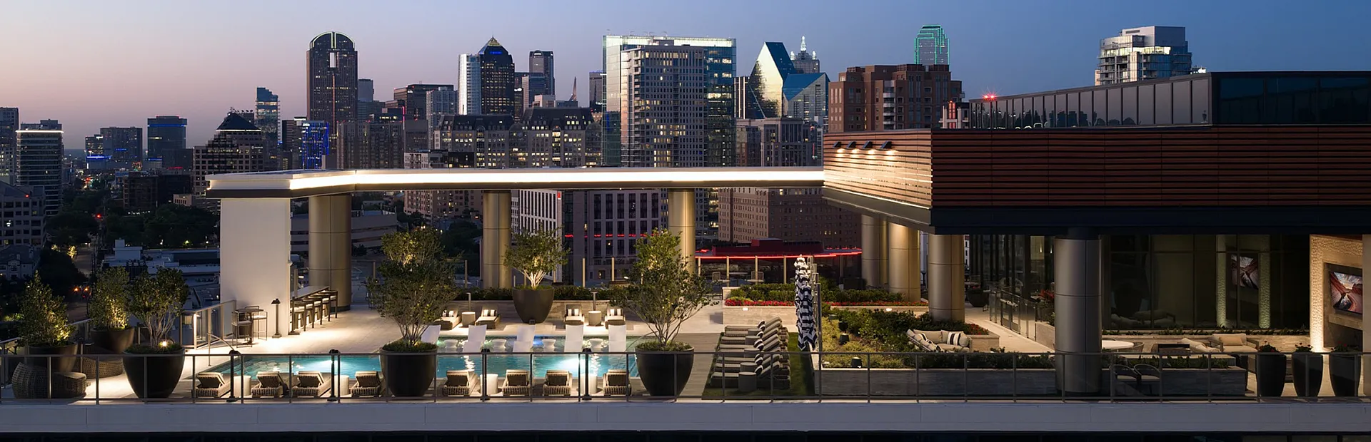 Luxurious rooftop terrace with modern lounge area and trees overlooking a vibrant cityscape at dusk.