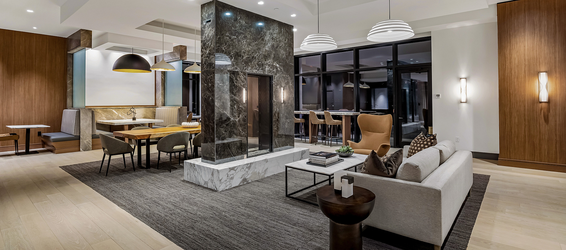 Luxurious open-concept living area with modern decor, featuring a double-sided marble fireplace, stylish dining nook, and ambient lighting.