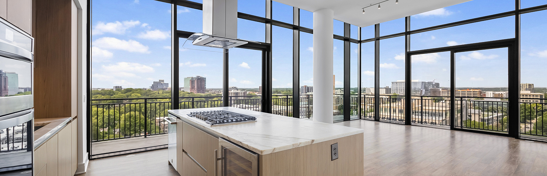 Luxurious modern kitchen with floor-to-ceiling windows offering stunning city views, featuring a sleek island and elegant hardwood floors.