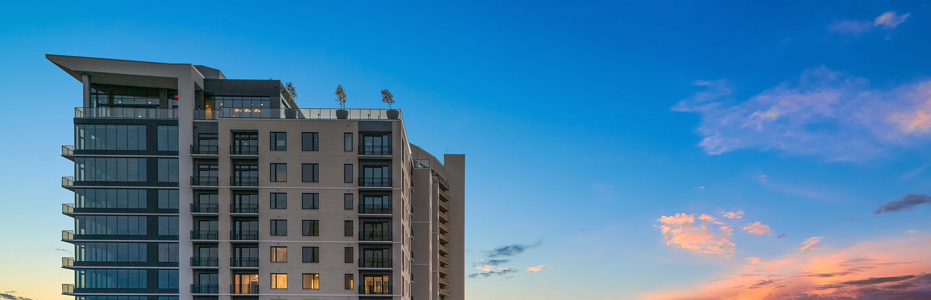 Stunning high-rise apartment building with modern design, featuring illuminated windows and a breathtaking sunset view.