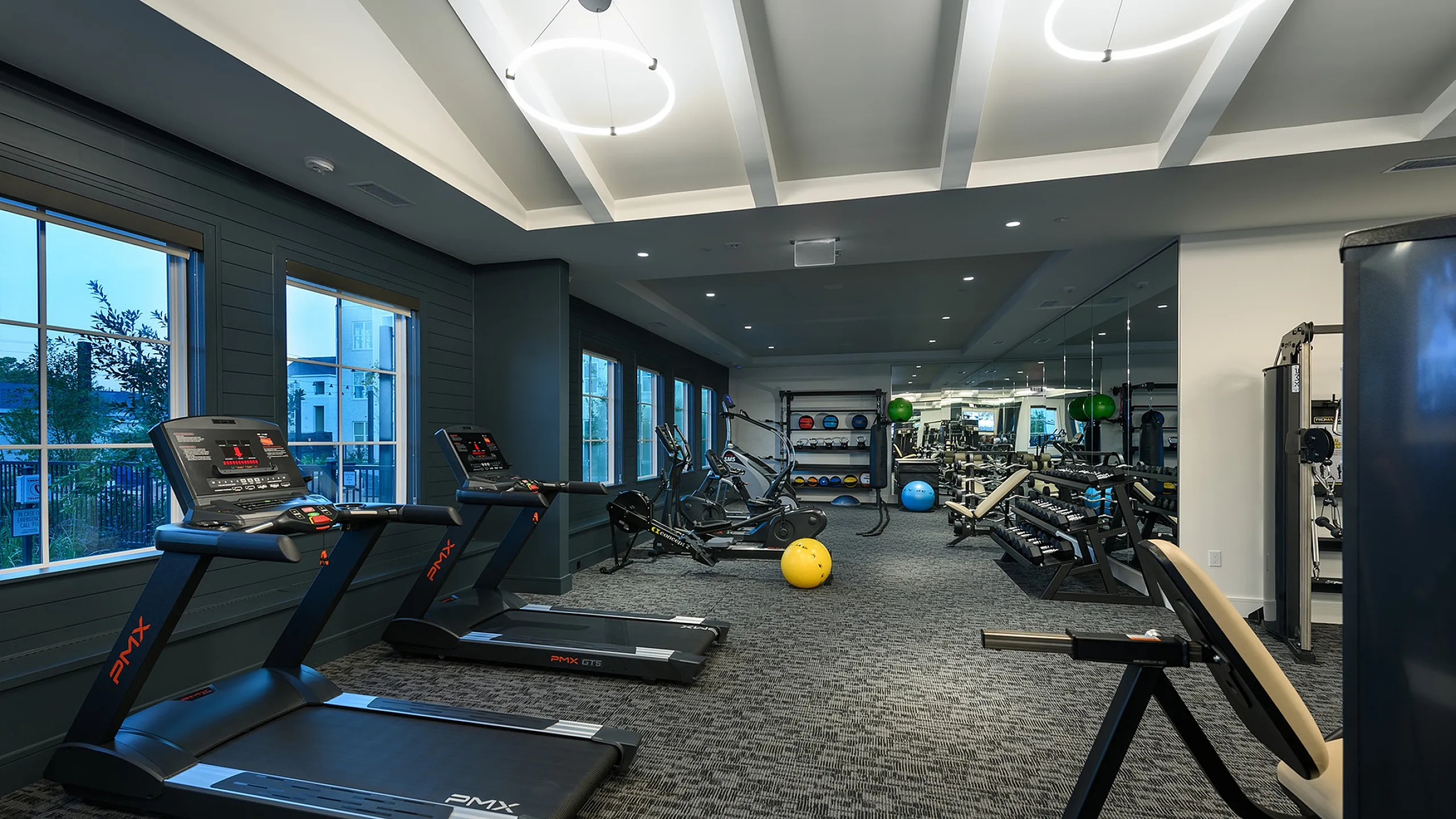 Modern and spacious fitness center with treadmills, exercise bikes, and a variety of strength training equipment, illuminated by stylish lighting and large windows with scenic views.