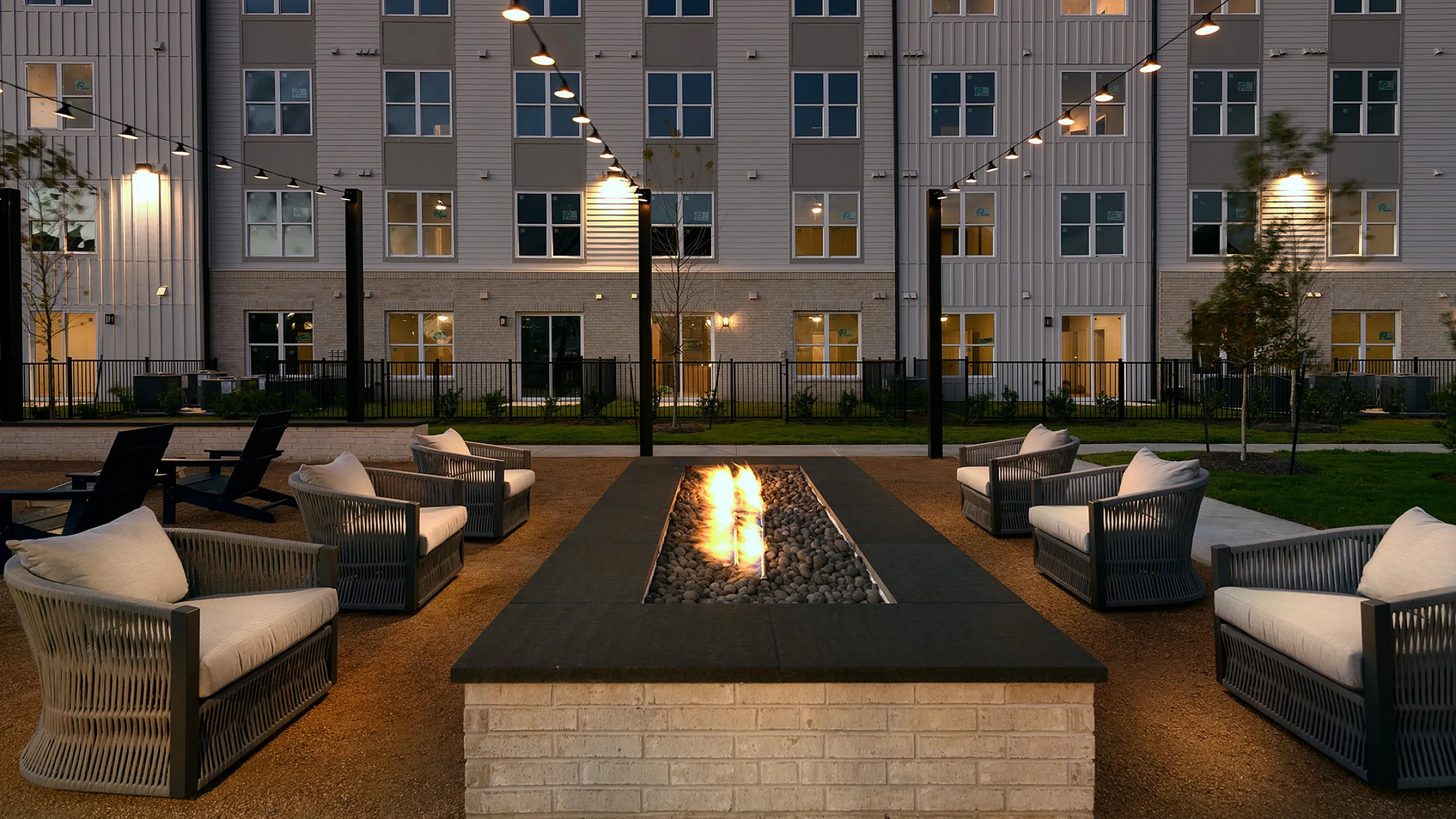 Chic outdoor communal area with cozy seating around a glowing fire pit, set against a modern apartment building facade.
