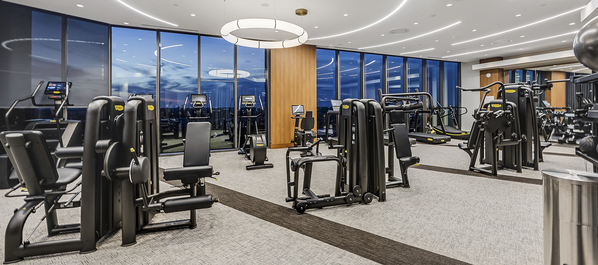 Modern fitness center with sleek exercise equipment and panoramic city views through large windows.