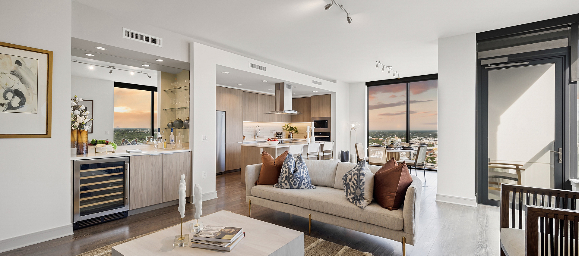 Luxurious open-concept apartment with elegant living area, modern kitchen, and stunning sunset views from floor-to-ceiling windows.