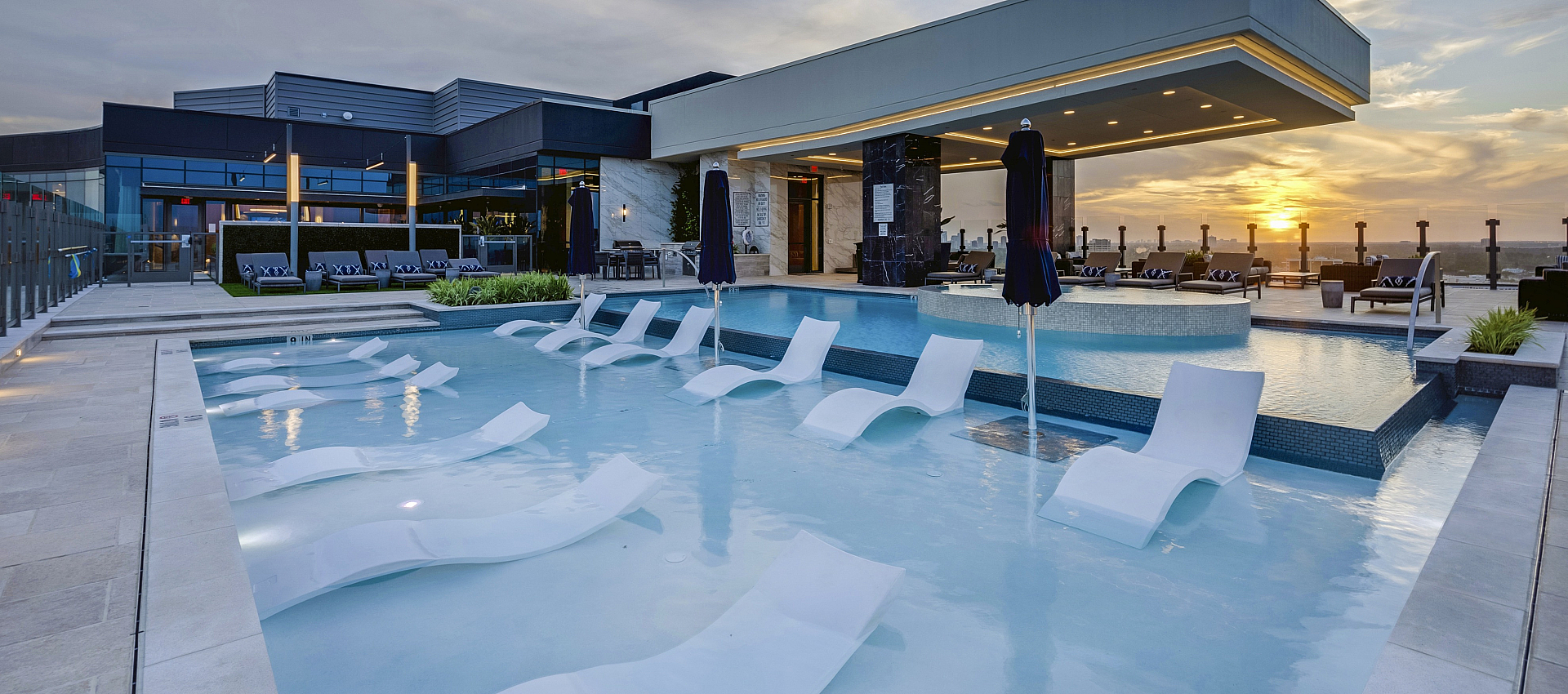 Luxurious rooftop pool with elegant lounge chairs, framed by stunning sunset views and modern architecture.