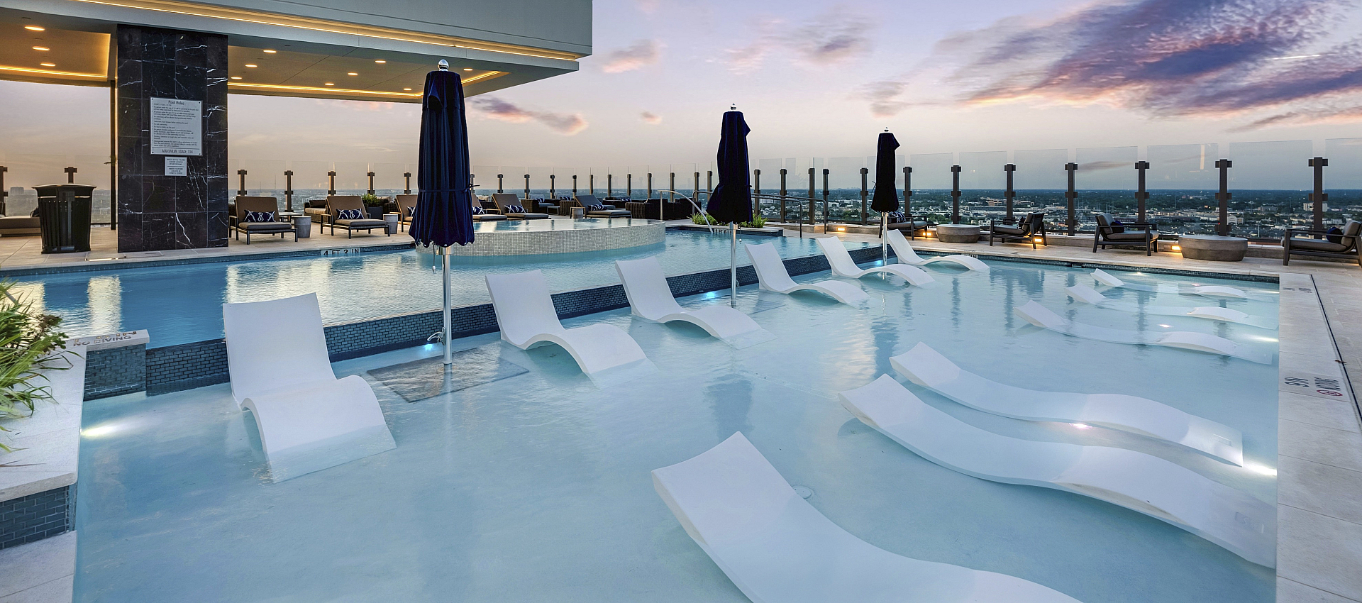 Elegant rooftop infinity pool offering stunning city views, with luxurious lounge chairs and ambient lighting against a beautiful sunset sky.