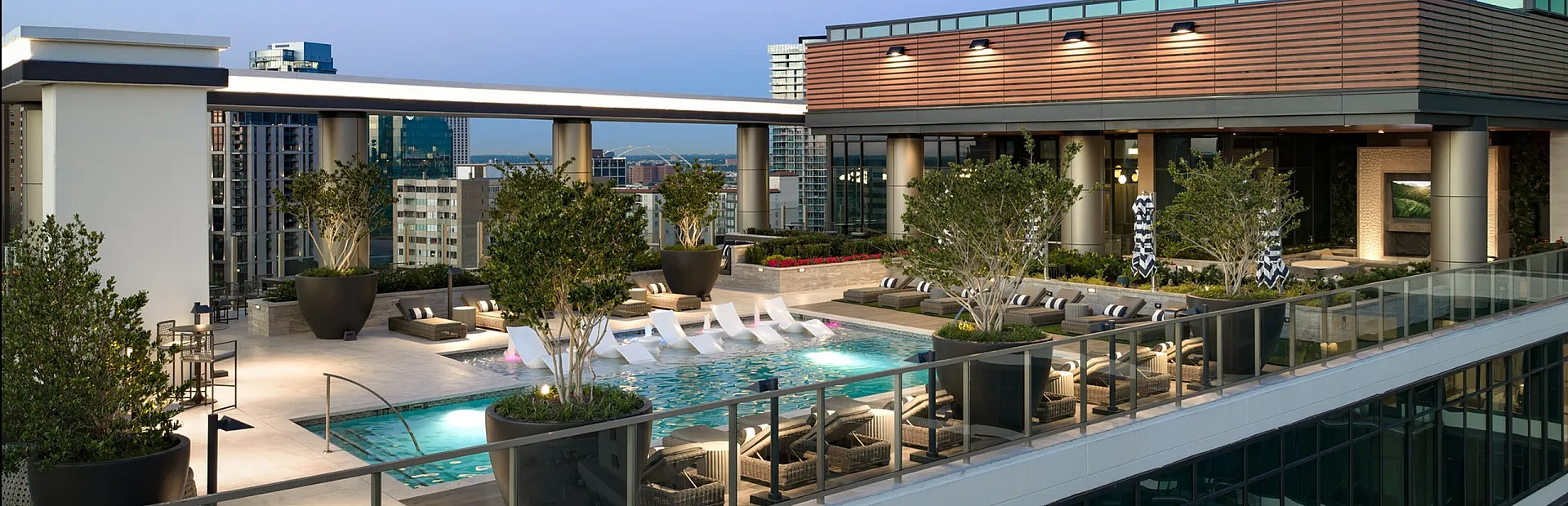 Luxurious rooftop view featuring an elegant pool surrounded by stylish lounge chairs and lush greenery, offering panoramic cityscape views.