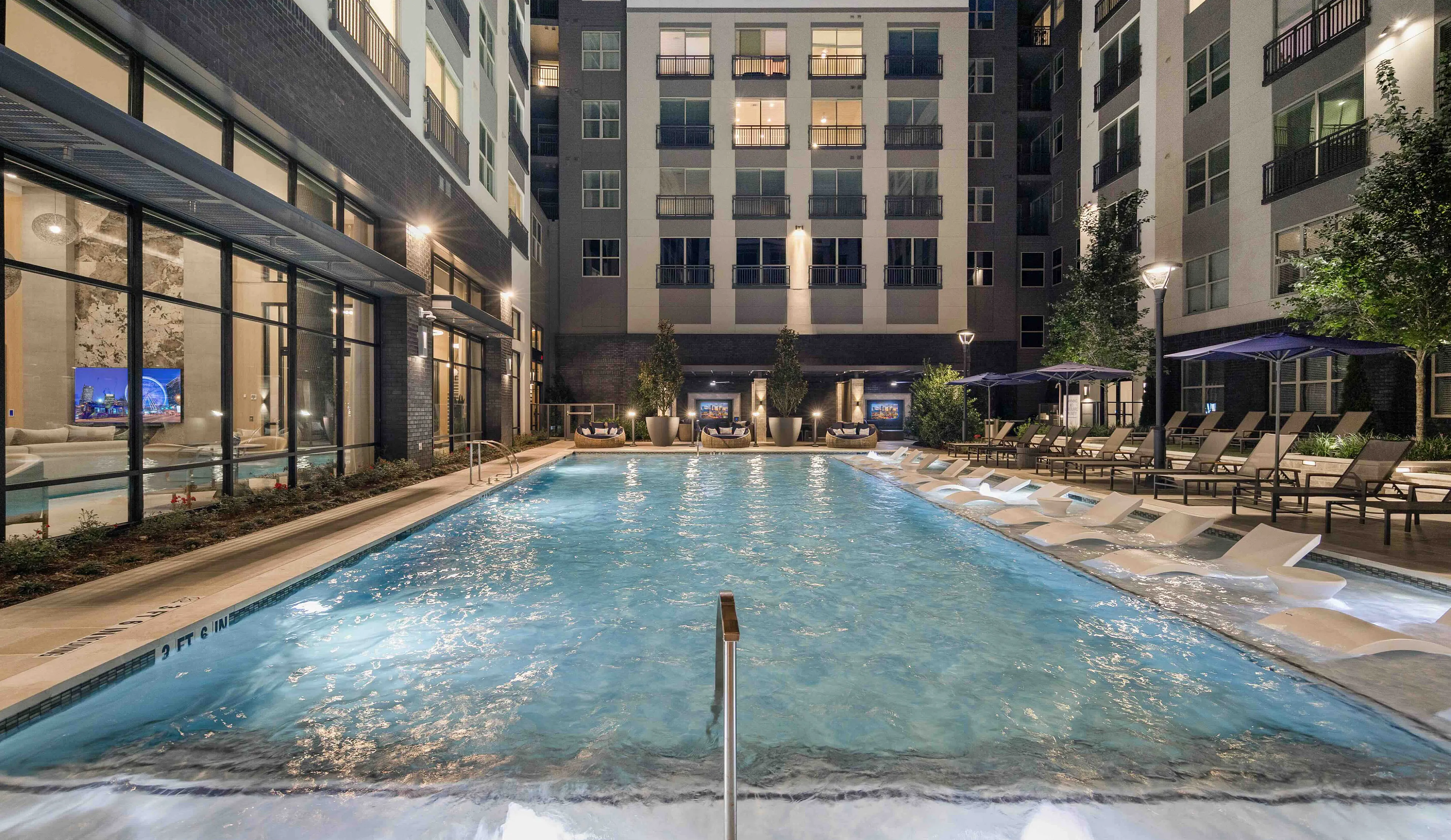 Luxurious apartment complex pool area with elegant lounge chairs and evening ambiance lighting.