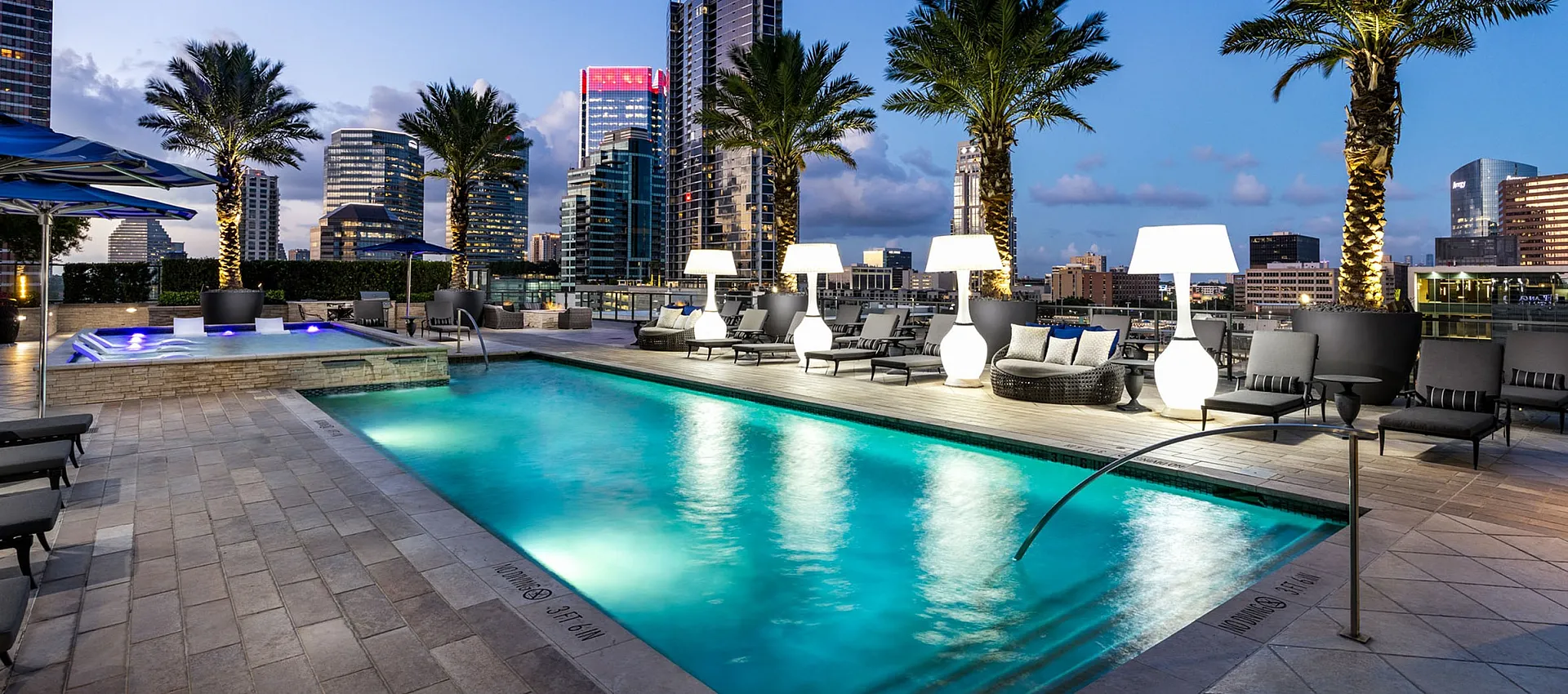 Luxurious rooftop pool with palm trees and city skyline views, featuring stylish lounge chairs and ambient lighting.