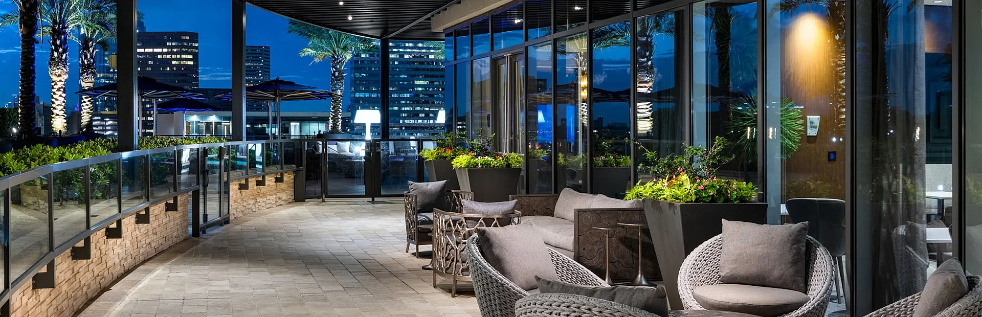 Elegant rooftop terrace at night featuring chic wicker seating, vibrant planters, and a stunning city skyline view.