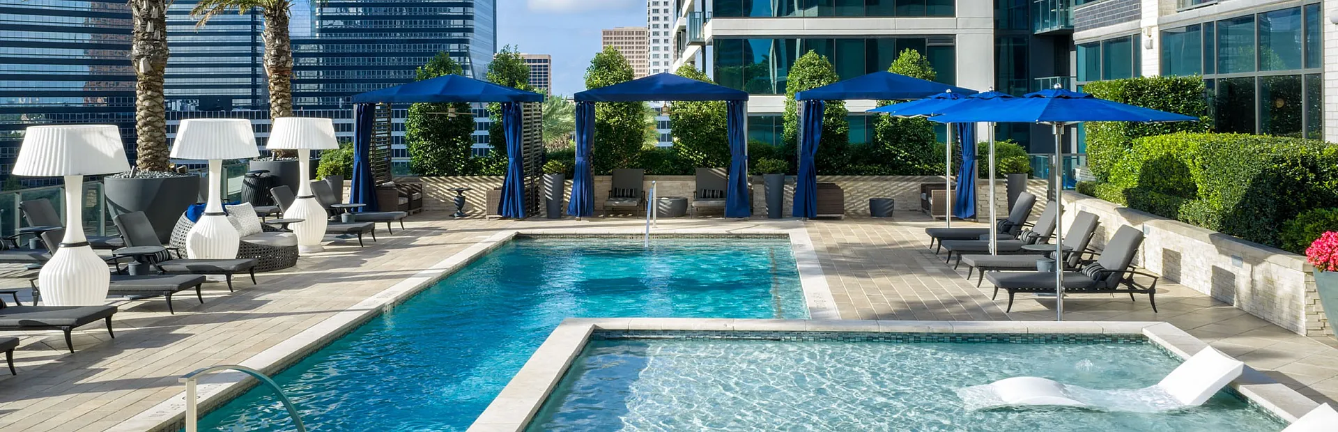Luxurious rooftop pool area with elegant seating, vibrant blue umbrellas, and stunning city views, offering a perfect relaxation spot.