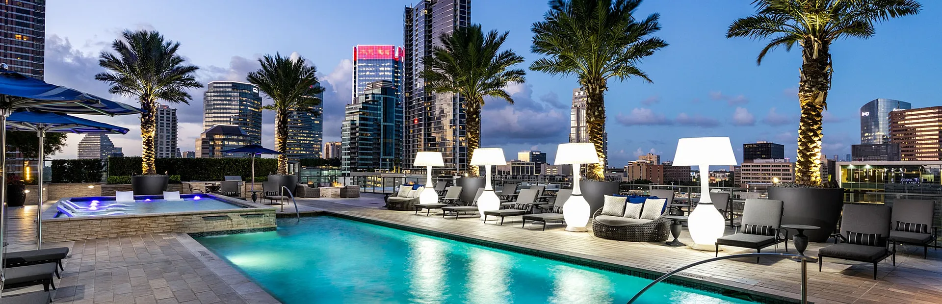 Luxurious rooftop pool with modern lounge chairs and palm trees, offering a stunning city skyline view.