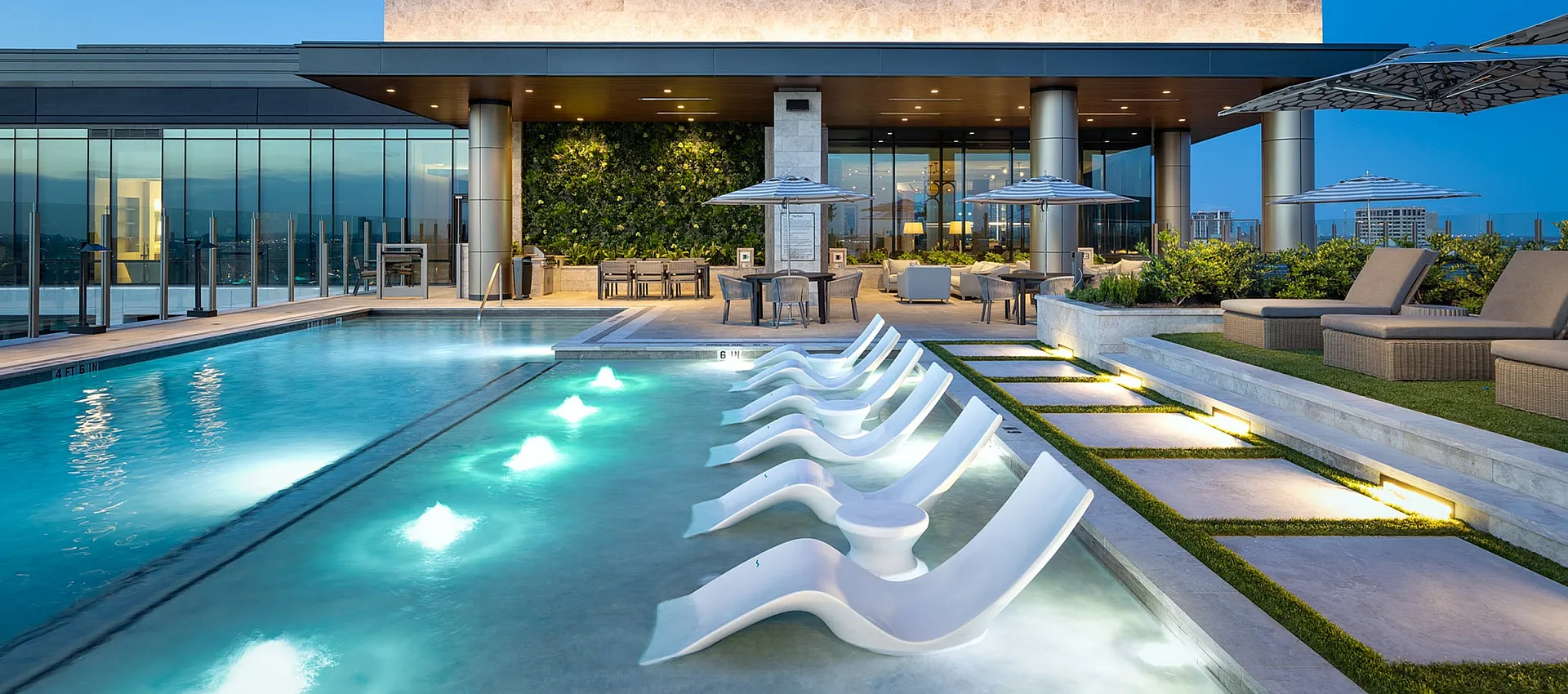 Luxurious rooftop pool with modern chaise lounges and ambient lighting, surrounded by sleek architecture and scenic city views.